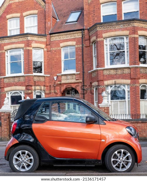 Barnes UK. March 2022. Bright orange eco friendly\
electric smart car parked outside brick building in Barnes, west\
London, UK.