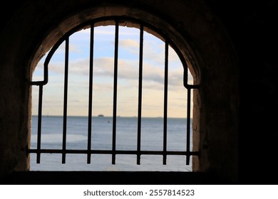 A barred window arch. Cast iron bars in an arched window, overlooking a blurred sea-sky horizon. - Powered by Shutterstock