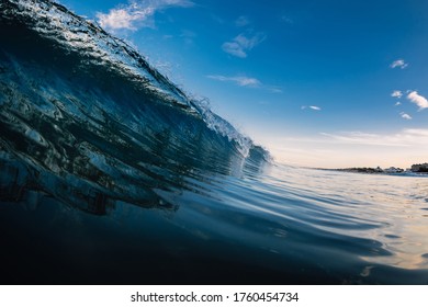 Barrel wave in ocean with sunrise tones and beach at background