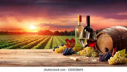 Barrel Wineglasses And Bottle In Vineyard At Sunset
