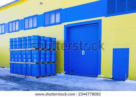 Barrels near industrial building. Hangar with blue gates. Warehouse area. Storehouse exterior. Factory building. Distribution center exterior. Concept - rent of industrial premises
