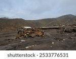 A barren and desolate landscape featuring an overturned and rusty car wreck amidst scattered debris showing the aftermath of  Merapi volcanic eruption. Illustrating the devastation caused by disaster.