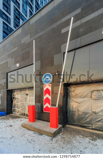 Barrier in front of closed gate\
to underground parking of residential complex of office. Sunny day\
in winter evening. Road signs parking and driving directions. \

