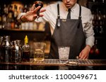 Bartender adding an alcoholic essence from a small glass bottle into the mixing glass on the bar counter