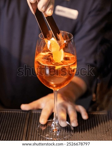 Bartender is adding the finishing touch to an aperol spritz cocktail by carefully placing an orange slice in the glass