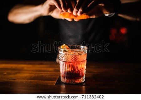 bartender with cocktail and orange peel preparing cocktail at bar. alcohol drinks, people and luxury concept