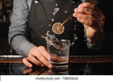 Bartender Decorating A Clear Glass Filled With Splashing Alcoholic Drink Using A Slice Of Lemon