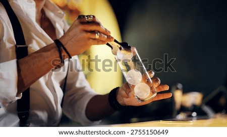 Bartender is dropping ice spheres into a glass, preparing a refreshing cocktail. Crafting drinks for nightlife