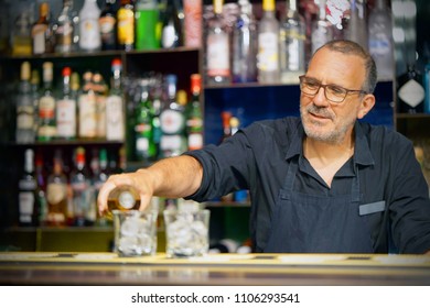 Bartender Elderly Man Pours Whiskey To The Client Of The Hotel Bar. The Concept Of Service. Focus On The Bartender.
