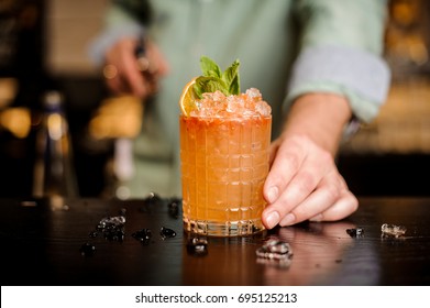Bartender finished decorating his cocktail with mint and orange slice