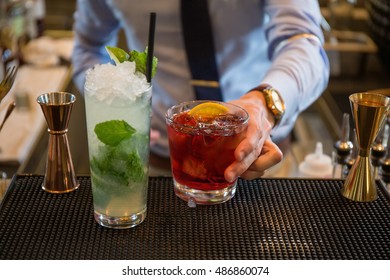 Bartender In Formal Dress Is Serving Cocktail Drinks Behind Bar Counter.