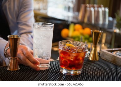 Bartender In Formal Dress Is Serving Cocktail Drinks Behind Bar Counter.