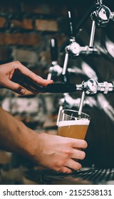 Bartender Hand At Beer Tap Pouring A Draught Beer In Glass In Tap Room