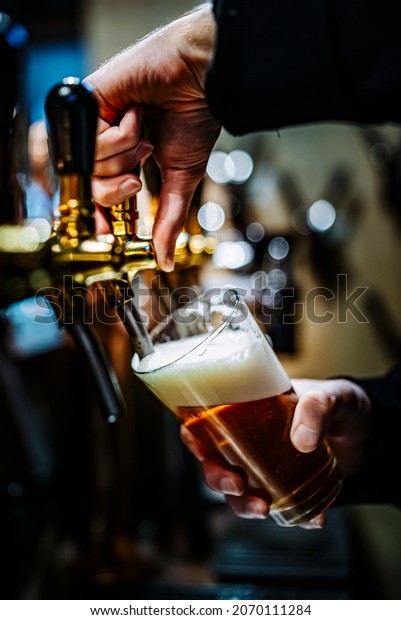 bartender hand at beer tap pouring a draught beer\
in glass serving in a bar or\
pub