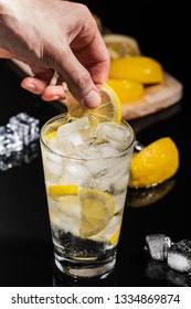 Bartender Hands Making Finish Details For Tasty Gin Tonic Mixed Drink Cocktail With Lemon Slices And Ice Cubes, On The Black Background