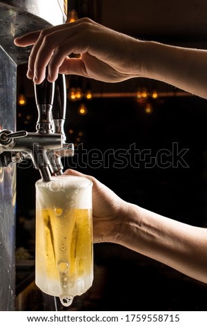 Bartender hands pouring a cold draft beer into a mug , black background. Pilsen