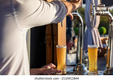 Bartender With His Hand On The Cold Brew Tap Serving A Draft Beer Outside On A Summer Day. Refreshing Cold Draft Beer Served On The Terrace To Withstand The Summer Heat