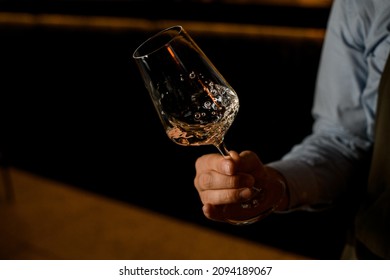 the bartender holds a glass of wine in his hands and stir it to make bubbles on the dark background