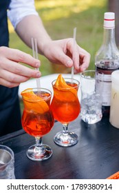 The Bartender Inserts Straws Into Orange Cocktails. Aperol Spritz In A Glass Tulip. Summer Party Catering. No Face.