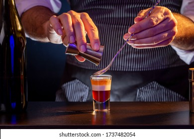 Bartender making B-52 layered cocktail, pouring irish cream from a measuring cup into a shot glass using cocktail spoon - Powered by Shutterstock