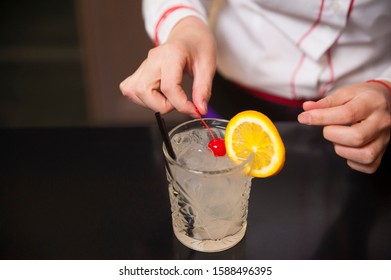 Bartender making refreshing Tom Collins coctail with orange slice and cherry on top 