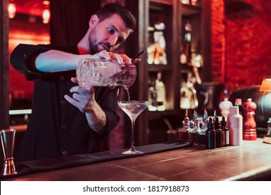 Bartender mixing cocktail. He is wearing black costume. He is in a pub. Bearded man. - Shutterstock ID 1817918873