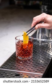 The Bartender On A Metal Bar Counter Makes A Cocktail Negroni In A Beautiful Glass.