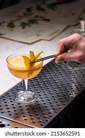 The Bartender On A Metal Bar Counter Makes A Cocktail In A Beautiful Glass.