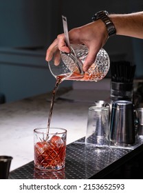 The Bartender On A Metal Bar Counter Makes A Cocktail Negroni In A Beautiful Glass.