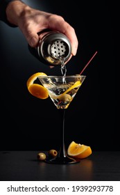 Bartender pour cocktail from shaker. Dry martini with lemon peel and green olives on a black background.
