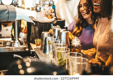 Bartender pouring alcohol from the bottle into the glasses - Happy friends group hanging out on weekend night at cocktail bar venue - Life style concept with barman making drinks and serves customers  - Powered by Shutterstock