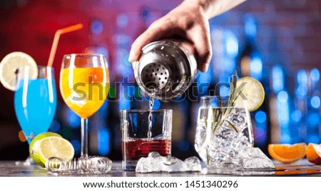 Bartender pouring cocktail into the glass. Set with different cocktails on a bar lights background.