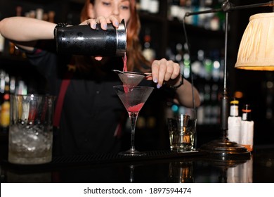 Bartender Pouring Cocktail From Shaker Into Glasses At Bar Counter In Bar