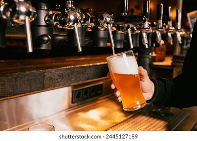 Bartender pouring light, cold foamy beer from tap into glass at bar with multiple beer dispensers. Serving craft beer from tap. Concept of alcohol drinks, nightlife, party, festivals, Oktoberfest. Ad - Powered by Shutterstock