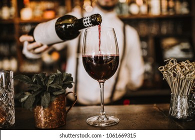 Bartender pouring red wine from a bottle in a wine glass, selective point of view on a wine glass