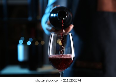 Bartender pouring red wine from bottle into glass indoors, closeup