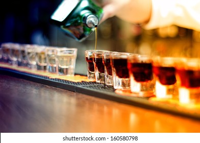 Bartender pouring strong alcoholic drink into small glasses on bar, shots