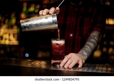 Bartender Pouring A Tasty Sippy Cup Cocktail From The Steel Shaker To A Glass With Big Ice Cube On The Bar Counter