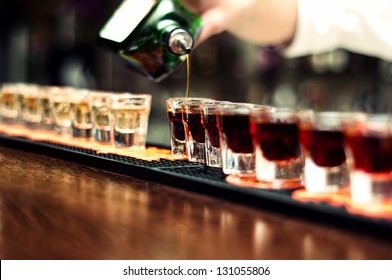 Bartender Pours Alcoholic Drink Into Small Glasses On Bar