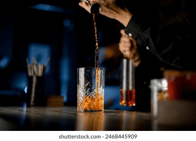 Bartender pours a brown alcoholic drink from a jigger into a tall cocktail glass - Powered by Shutterstock