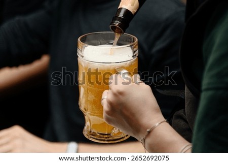 bartender pours light beer into large beer mug for customer at bar, close-up view of hand holding mug