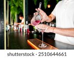 bartender pours pink cocktail into an elegant glass at a modern bar, highlighting mixology and nightlife. scene captures art of cocktail preparation with a focus on vibrant drink and stylish setting.