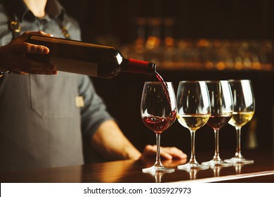 Bartender pours red wine in glasses on wooden bar counter - Shutterstock ID 1035927973