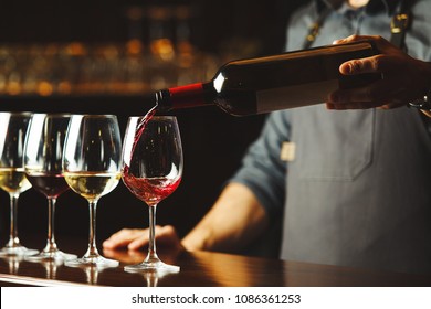 Bartender pours red wine in glasses on wooden bar counter - Powered by Shutterstock