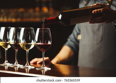 Bartender pours red wine in glasses on wooden bar counter - Powered by Shutterstock