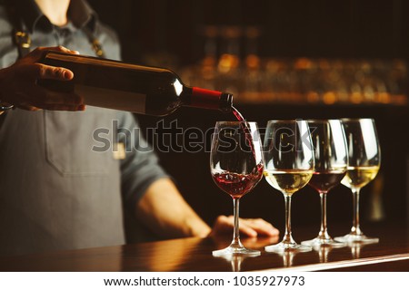 Bartender pours red wine in glasses on wooden bar counter