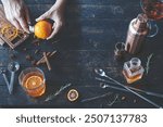 Bartender preparing a cocktail with fresh orange, spices, and a cocktail shaker, showcasing a vibrant setup on a rustic wooden table.