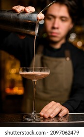 Bartender Professionally Pours Brown Cocktail From Shaker Into Glass Standing On Metal Bar Counter