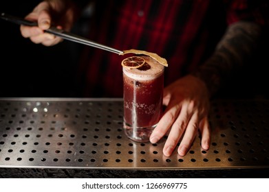 Bartender Putting A Dried Orange To A Sippy Cup Cocktail In The Glass With Tweezers On The Bar Counter