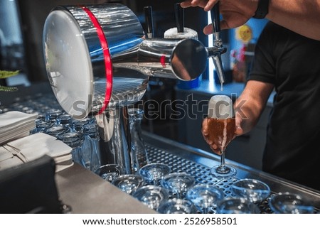 A bartender skillfully pours a fresh draft beer into a glass at a contemporary bar. The setting captures a casual and inviting atmosphere, ideal for social gatherings and relaxation.